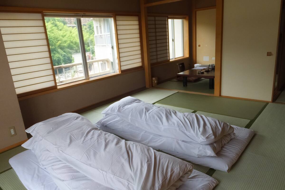 A traditional Japanese room with tatami flooring, a low table, and two beds with white bedding.