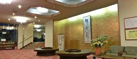 A lobby with a red carpet, a reception desk, a seating area with sofas, and a large wall-mounted sign.