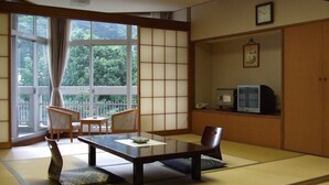 A traditional Japanese room with tatami flooring, a low table with a remote control, and a television on a shelf. - Itoen Hotel Shikisai (Yugawara)