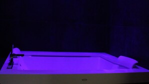 Un cuarto de spa con una bañera grande, piso de madera e iluminación empotrada en el techo.