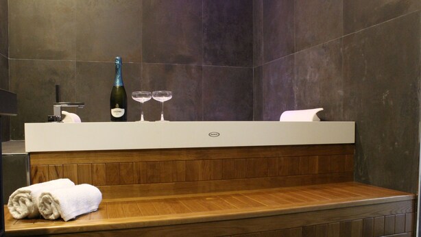 Un baño moderno con un banco de madera, un perchero y una botella de champán sobre una encimera.