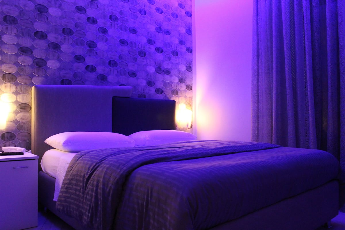 Un dormitorio con cama, mesita de noche y lámpara en la pared.