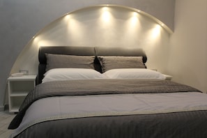 Un dormitorio moderno con cabecera curva, una mesita de noche y una cama bien tendida con muchos almohadones.