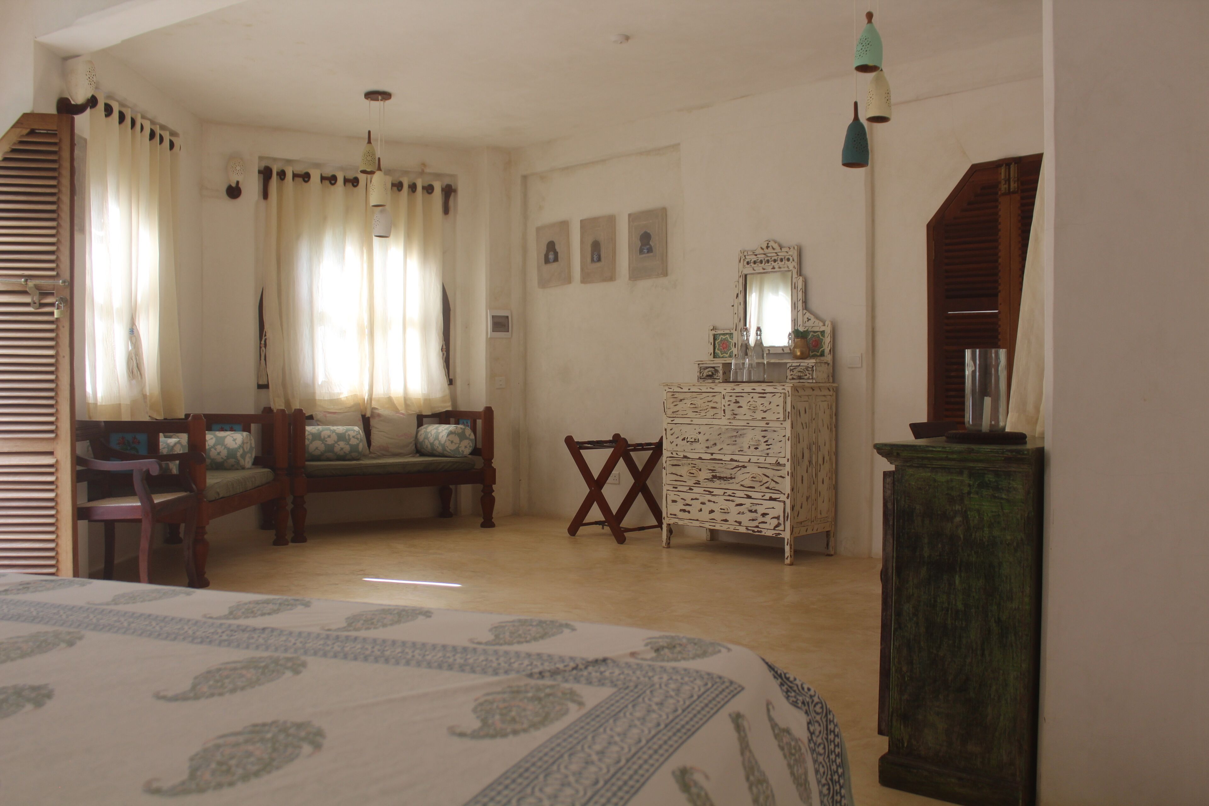A room with a bed, a wooden chair, a small table, a dresser, and a mirror.
