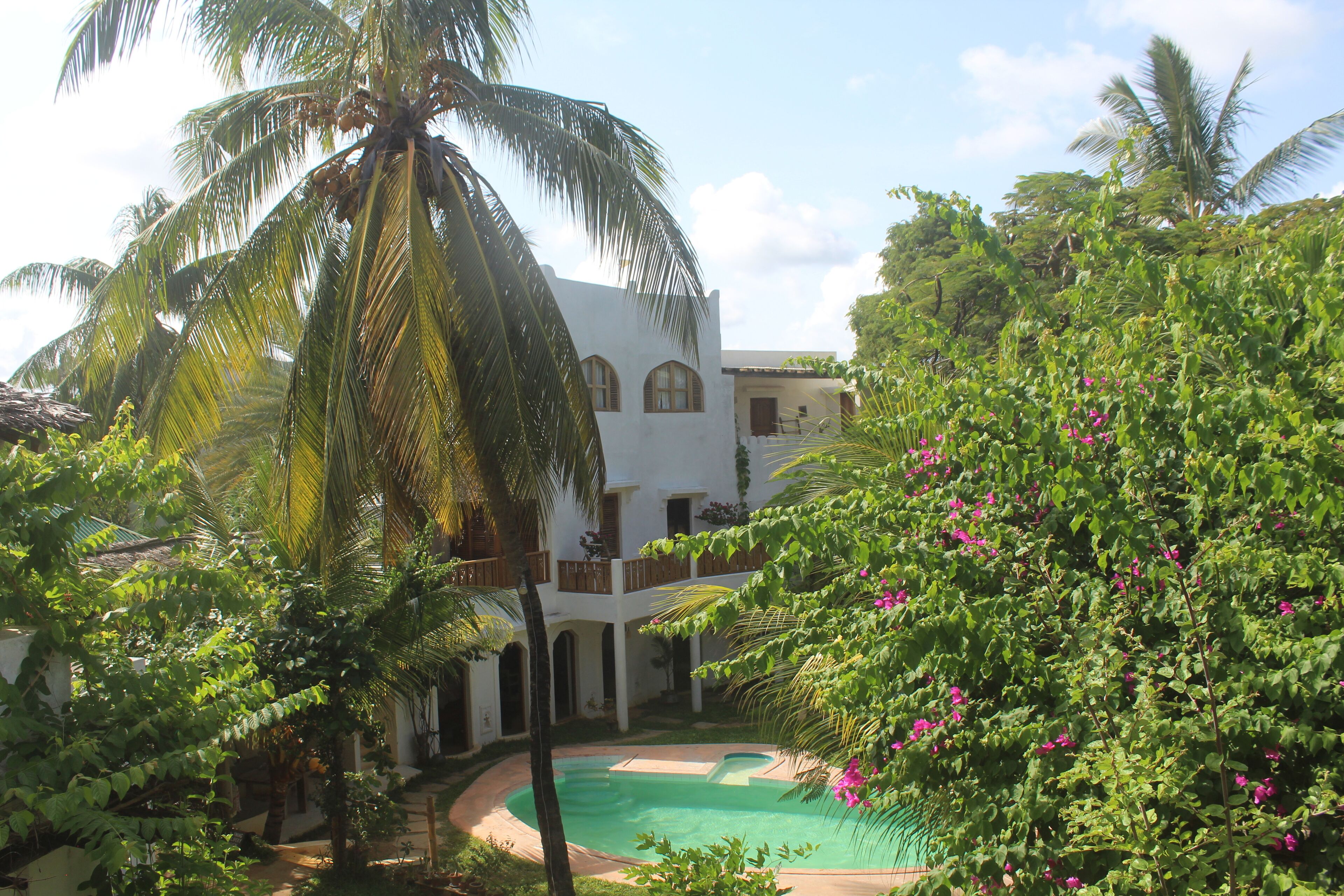 A white building with arched windows and a pool surrounded by lush greenery and palm trees.