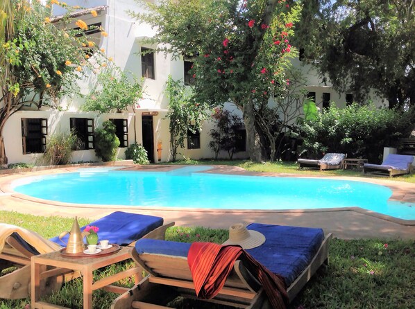 Una piscina con sillones de descanso y una mesa con un sombrero y un jarrón de flores.