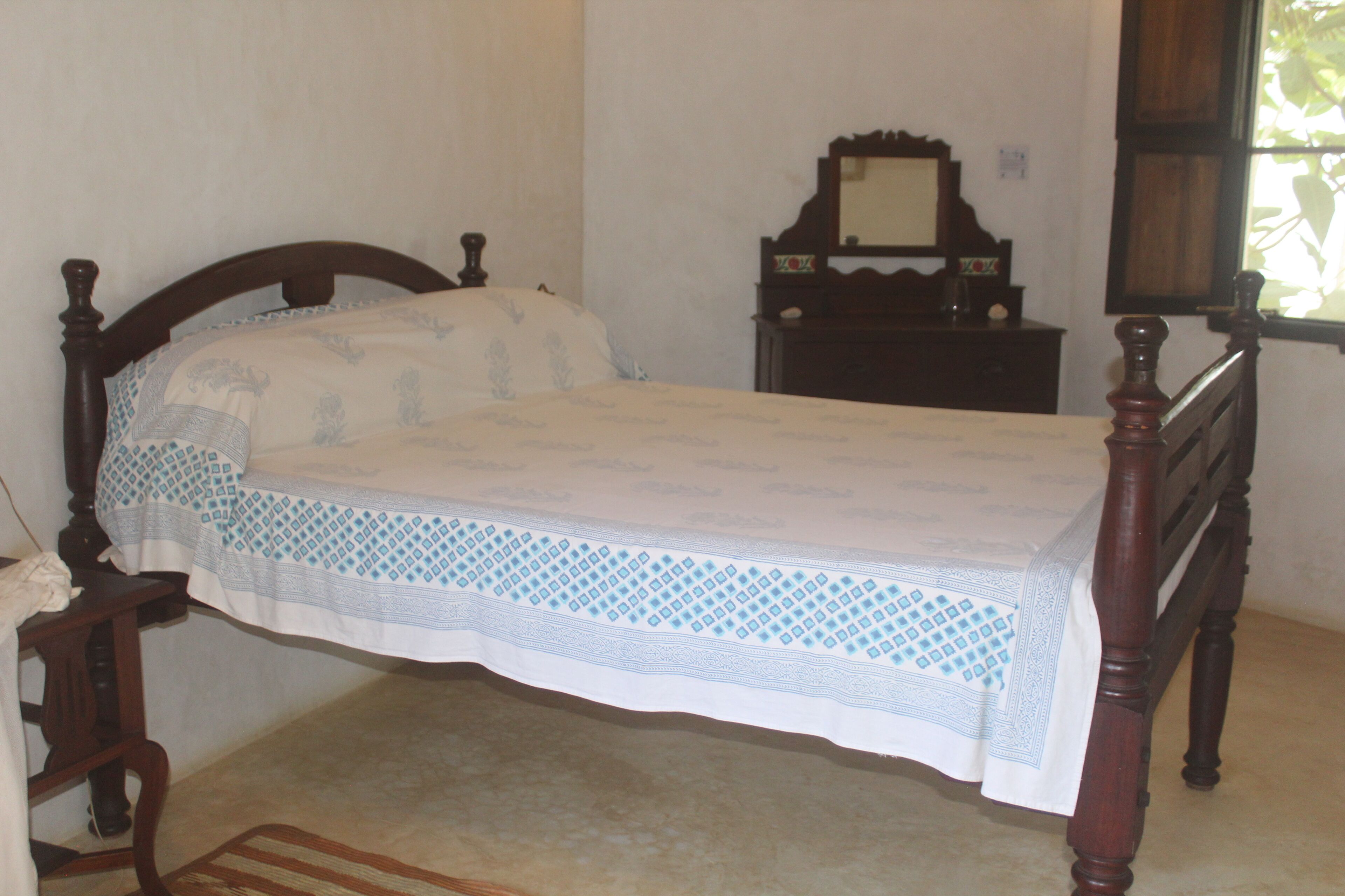 Een slaapkamer met een houten bed, nachtkastje, dressoir en spiegel.