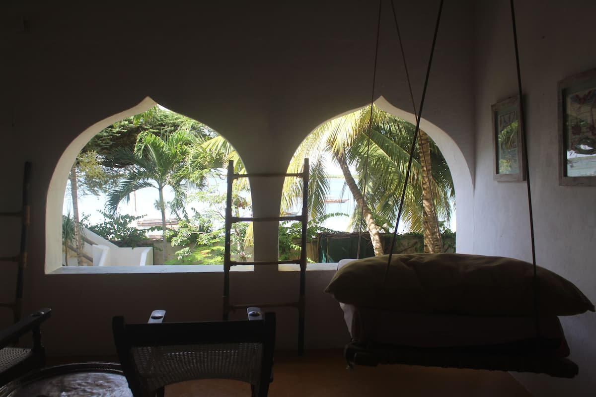 A room with a bed, a chair, and a window with a view of palm trees.