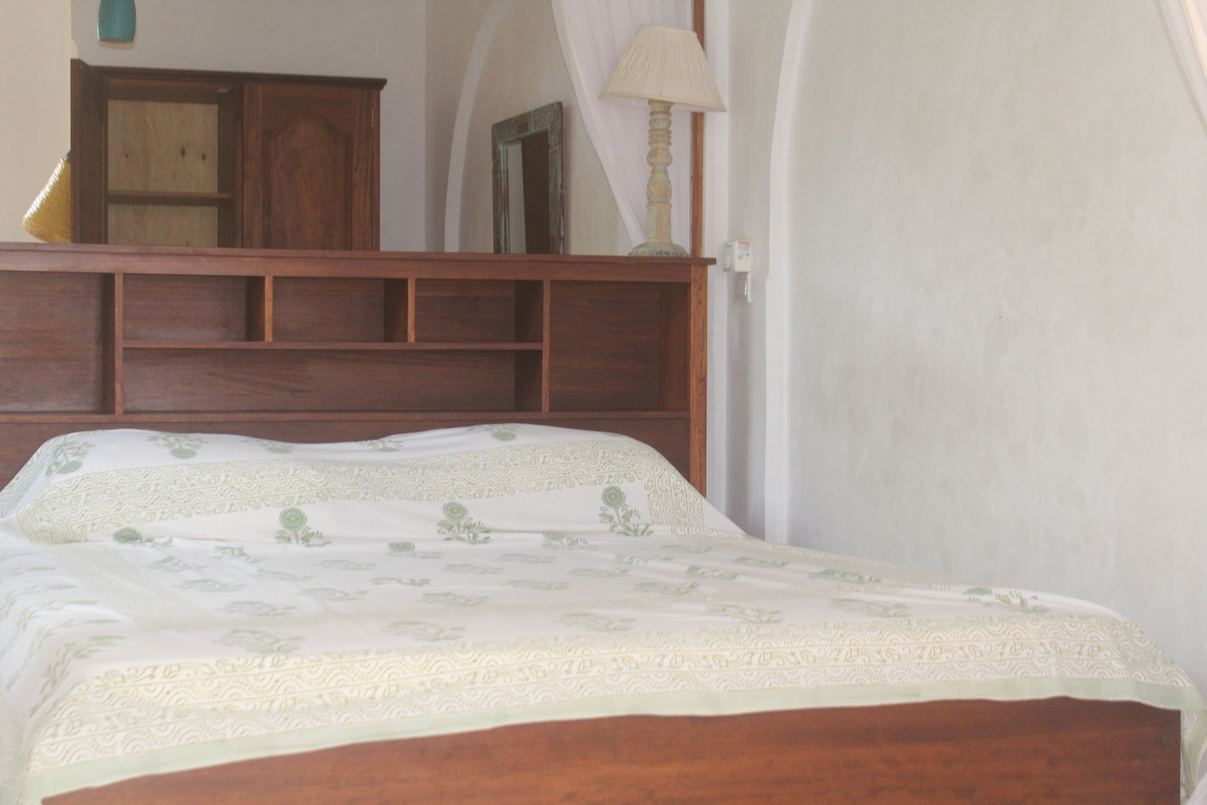 Un dormitorio con cabecera de madera, cama con colcha floral, mesita de noche y una lámpara.