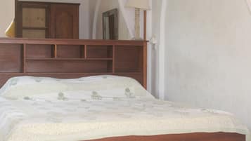 Un dormitorio con cabecera de madera, cama con colcha floral, mesita de noche y una lámpara.