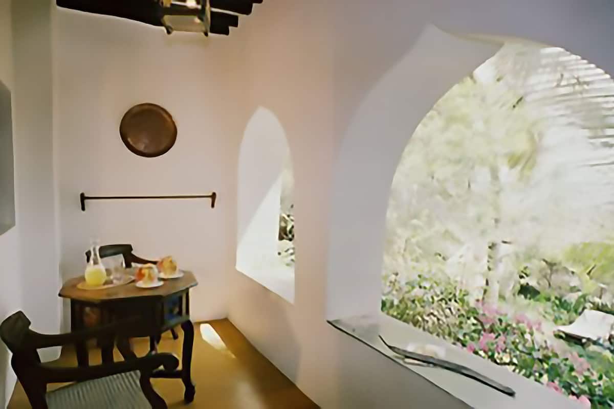 A room with a table set for two, a hanging light fixture, and a view of a garden through a large window.