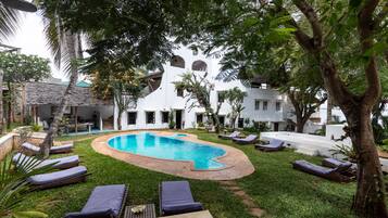 A pool area with lounge chairs, a white building with arched windows, and lush greenery.