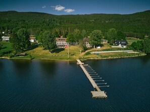 Vista aérea de una propiedad junto al lago con un muelle que se extiende hacia el agua, rodeada de abundante vegetación y viviendas.