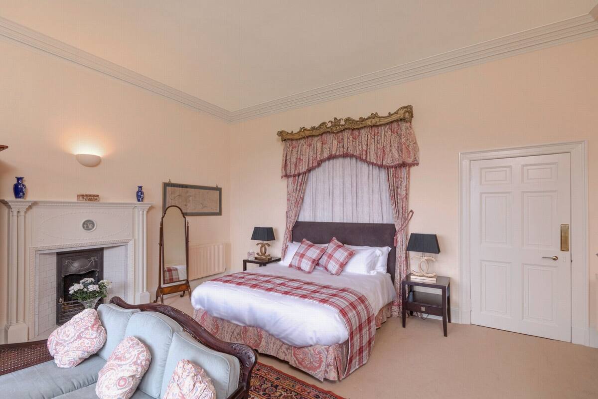 Quarto com cama grande, lareira, mesa de cabeceira com abajures e uma porta.