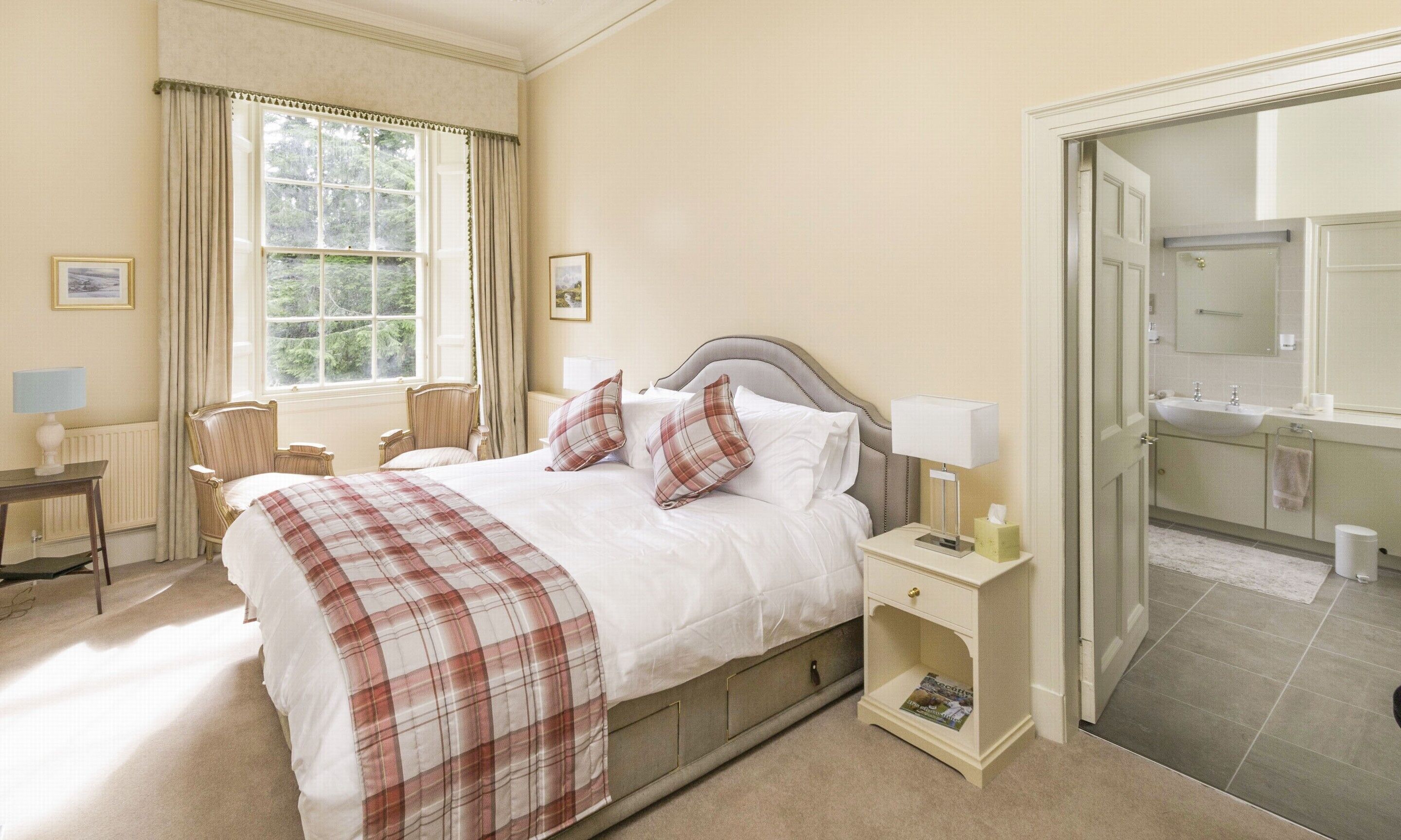 A neatly arranged bedroom with a bed, bedside tables, a chair, and a view of the bathroom through an open door.