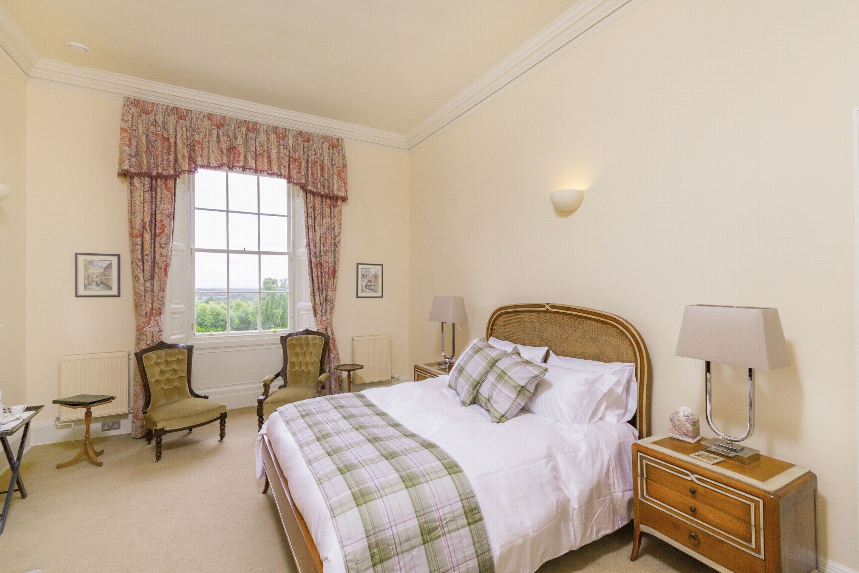 A neatly arranged bedroom with a bed, two chairs, a bedside table, and a lamp.
