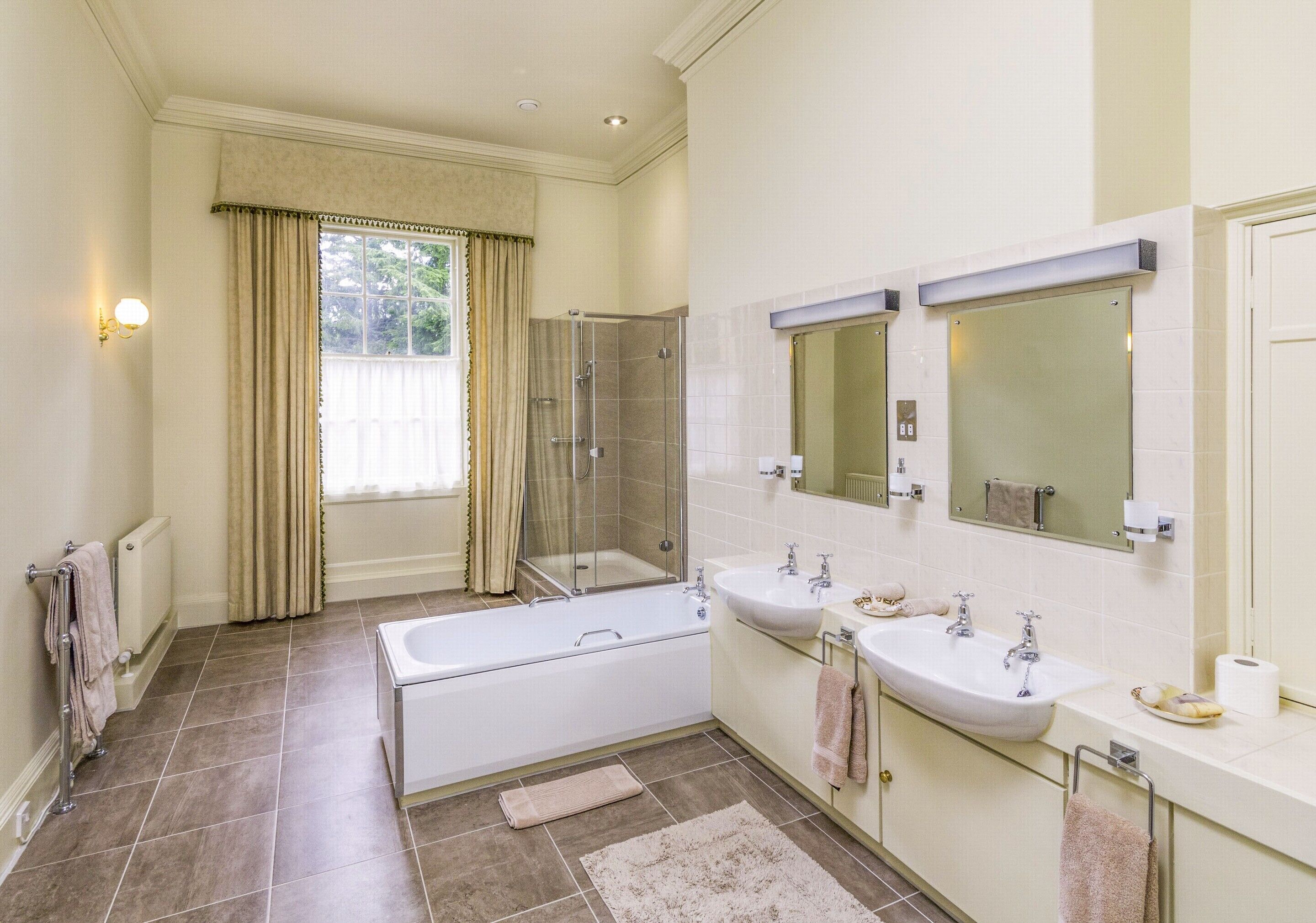 Un baño moderno con bañera, dos lavamanos, cabina de ducha de cristal y un espejo grande.