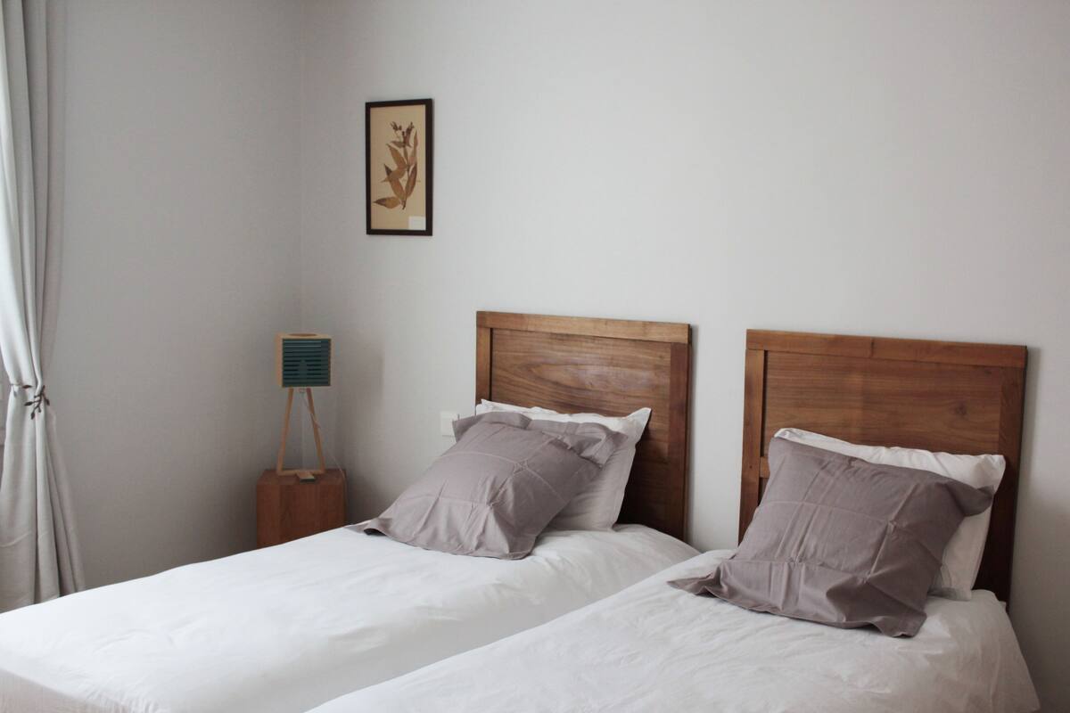A bedroom with two beds, each with wooden headboards and grey bedding.