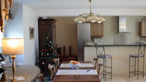 A dining area with a wooden table, chairs, a Christmas tree, and a kitchen in the background. - Chez Juliette Maison Gîte (Rontignon)