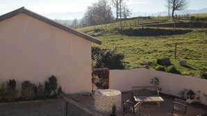 A patio with a stone wall, a wooden bench, and a small table. - Chez Juliette Maison Gîte (Rontignon)