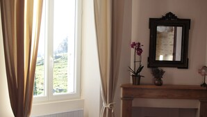 A room with a fireplace, a mirror, and a window with curtains. - Chez Juliette Maison Gîte (Rontignon)