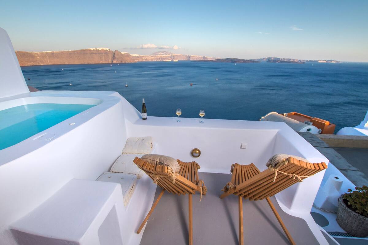 Une terrasse ensoleillée avec une piscine, deux chaises longues en bois et une vue sur la mer et les falaises.