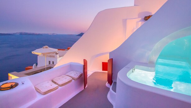 A modern hotel room with a large glass bathtub, a sun terrace with a view of the sea, and a white architectural design. - Hector Cave House (Santorini)
