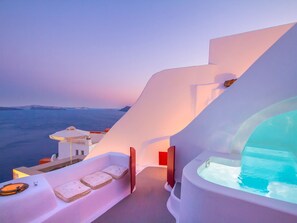 Una habitación de hotel moderna con una amplia bañera de vidrio, una terraza soleada con vistas al mar y un diseño arquitectónico en blanco.