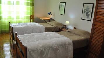 A room with two single beds, a desk, a chair, a lamp, and two framed pictures on the wall.