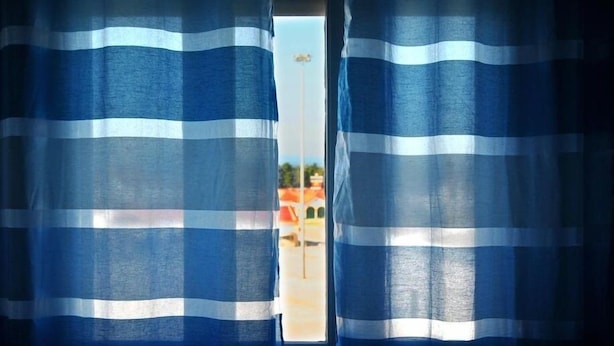 A window with blue and white striped curtains, revealing a view of a building and a clear sky. - Tagus Host (Santarém)