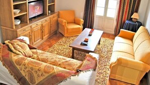 A cozy living room with a sofa, armchair, coffee table, and a television on a wooden cabinet. - Tagus Host (Santarém)