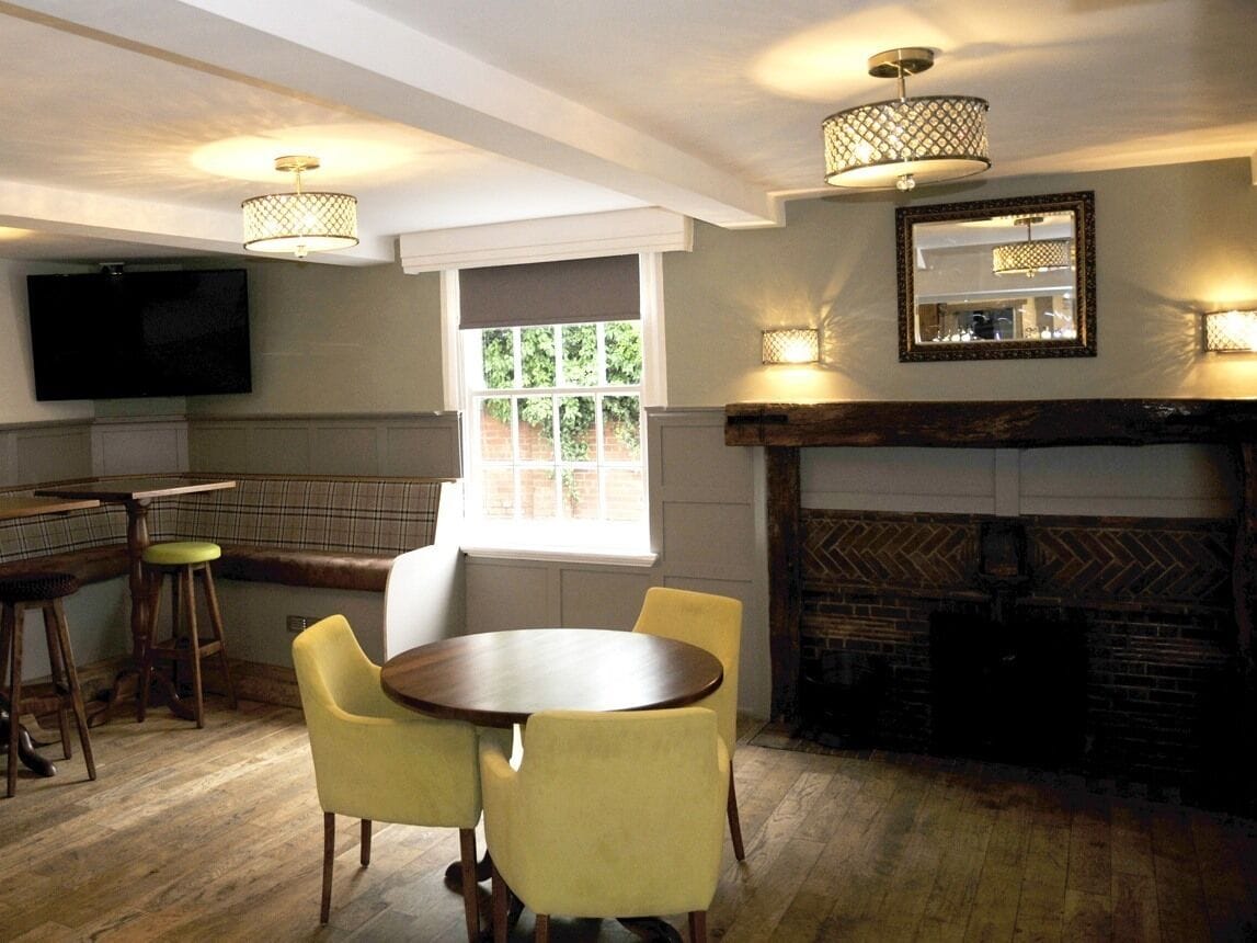 A dining area with a round table, yellow chairs, a fireplace, and a television mounted on the wall.