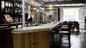 Una zona de bar con mostrador de madera, múltiples grifos y una disposición de asientos con sillas.