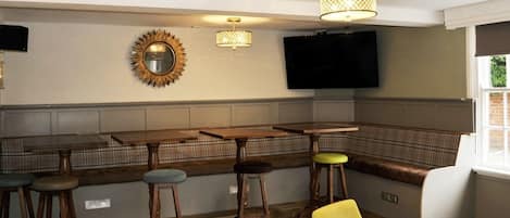 Un espace bar avec des tabourets en bois, un banc et un téléviseur fixé au mur.