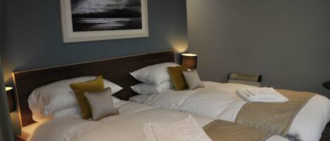 A hotel room with two beds, a framed picture on the wall, a bedside lamp, and a flat-screen TV.