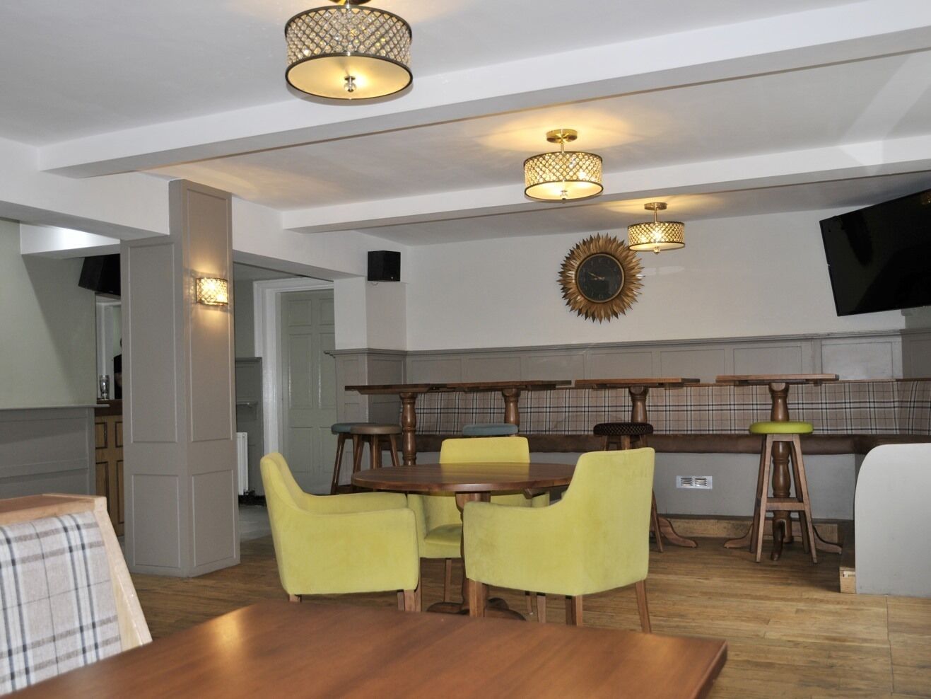 A modern dining area with a wooden table and yellow chairs, a bar area with stools, and pendant lighting fixtures.