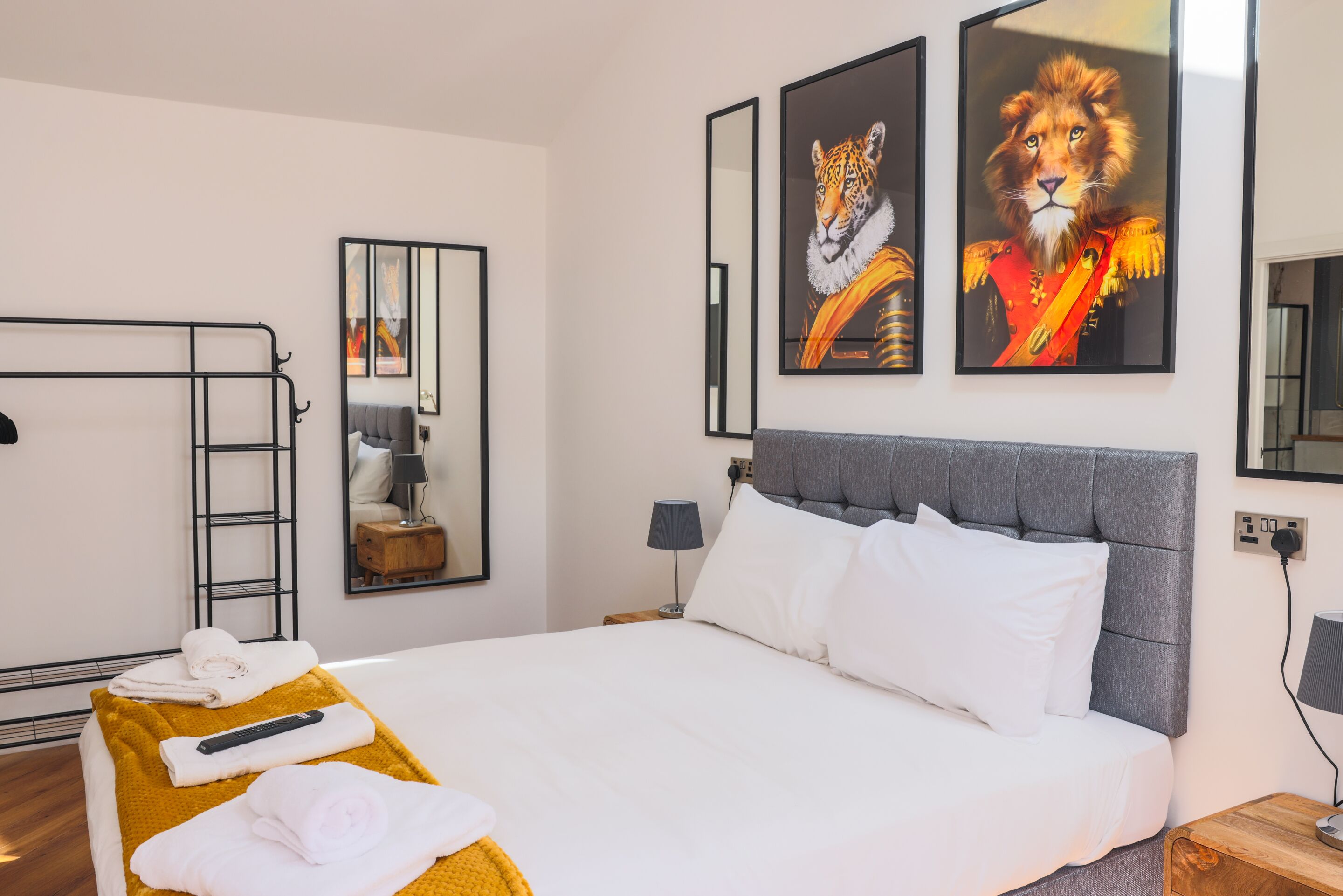 A hotel room with a large bed, a bedside table, a mirror, and artwork of tigers and lions on the wall.