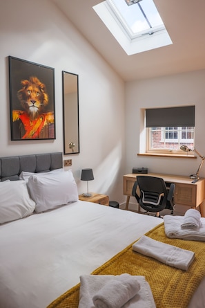 Relax in a stylish room with a large bed, desk, and window offering a view of a nearby brick building.