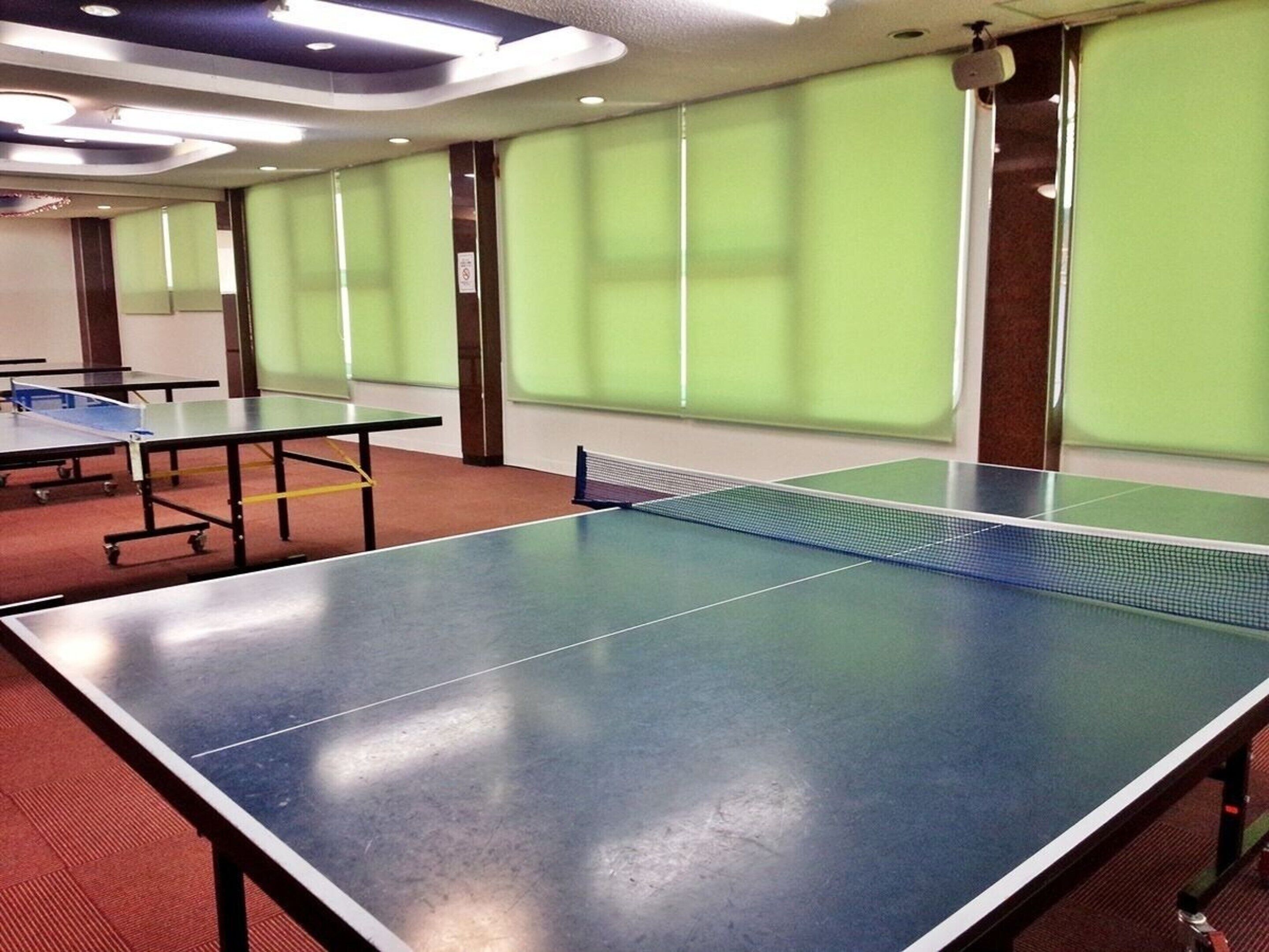 Een kamer met pingpongtafels en groene scheidingswanden.