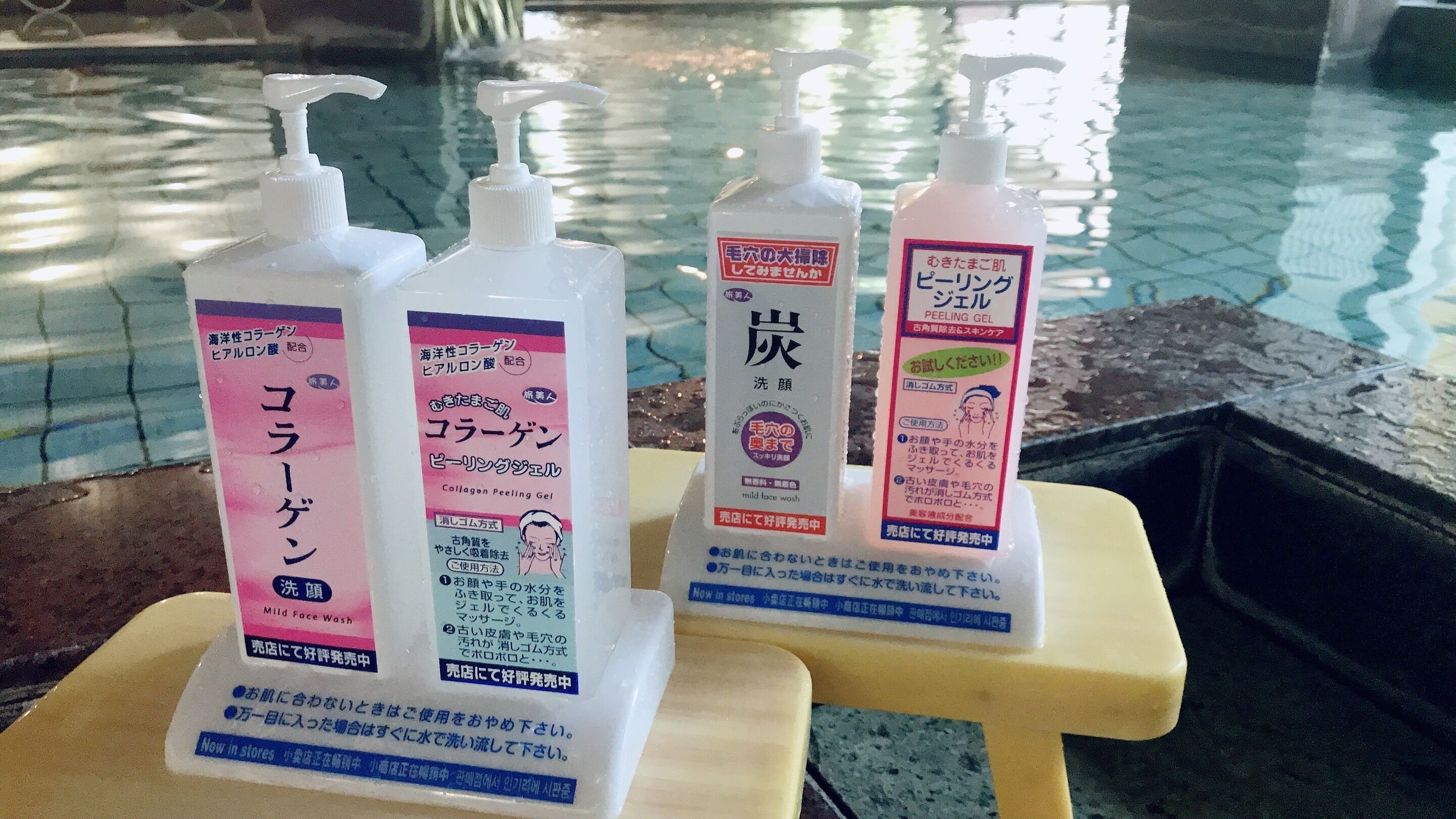 Tres botellas de productos para el cuidado de la piel sobre un taburete junto a una piscina.