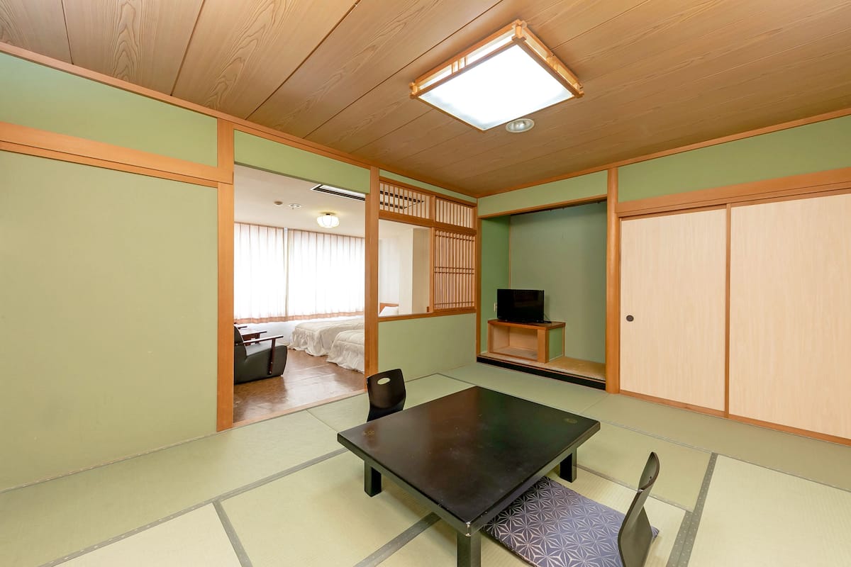 Ett traditionellt japanskt rum med tatamimattor på golvet, ett lågt bord, en tv på en hylla och skjutdörrar.