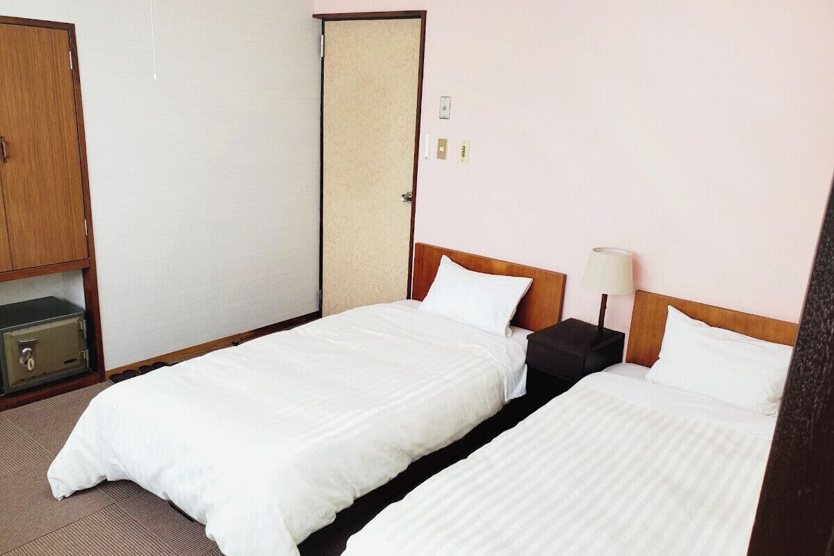 Ett hotellrum med två separata sängar, en sänggavel i trä, ett nattduksbord med en lampa och ett värdeskåp.