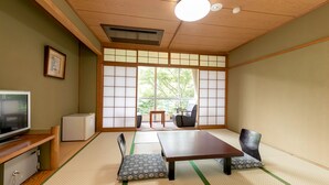 Una habitación japonesa tradicional con suelo de tatami, una mesa baja, sillas, televisor y refrigerador.