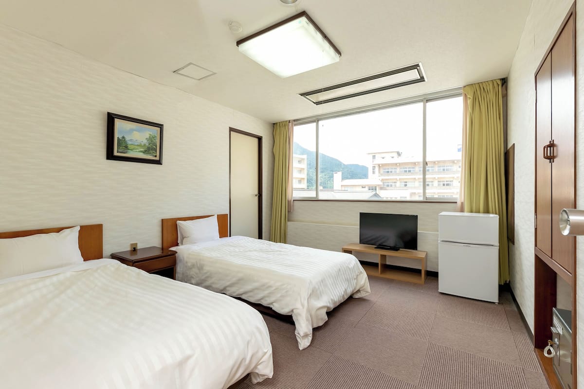 Ett hotellrum med två sängar, en tv, ett kylskåp och ett fönster med gardiner.