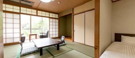 A traditional Japanese room with tatami flooring, a low table with chairs, a bed with white bedding, and sliding doors.
