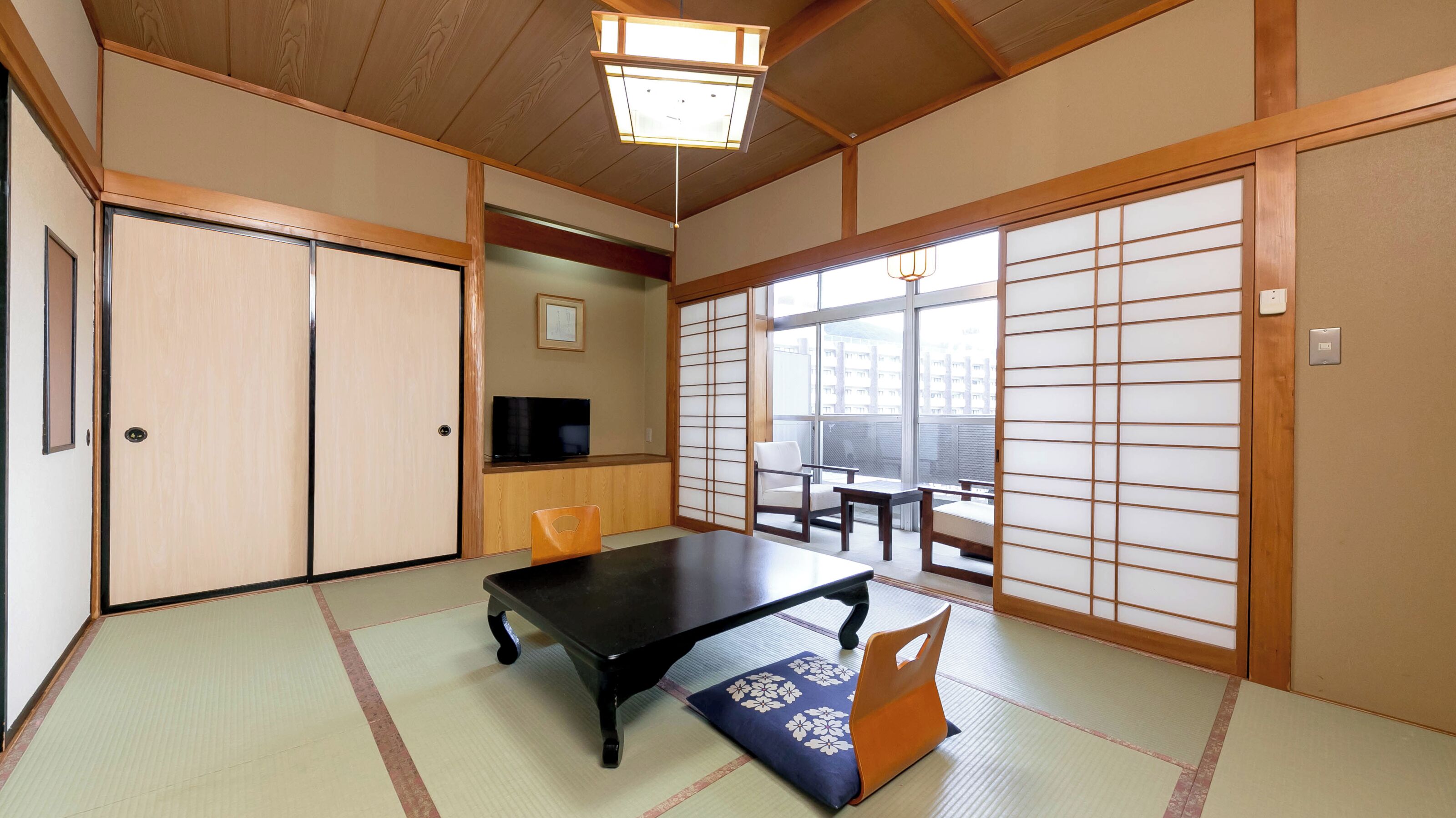 A traditional Japanese room with tatami flooring, a low table, sliding doors, and a television.