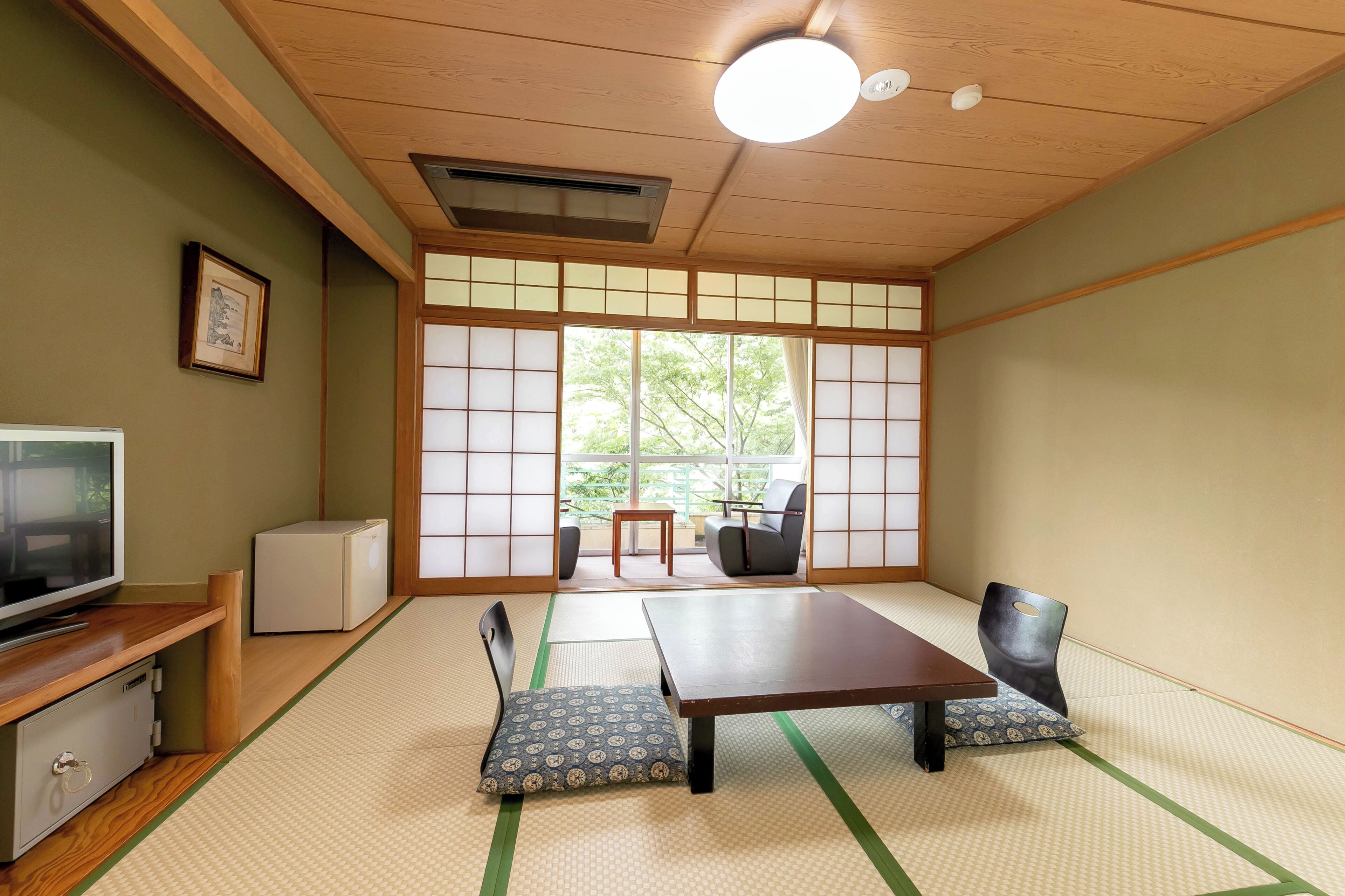 A traditional Japanese room with tatami flooring, a low table, chairs, a television, and a refrigerator.