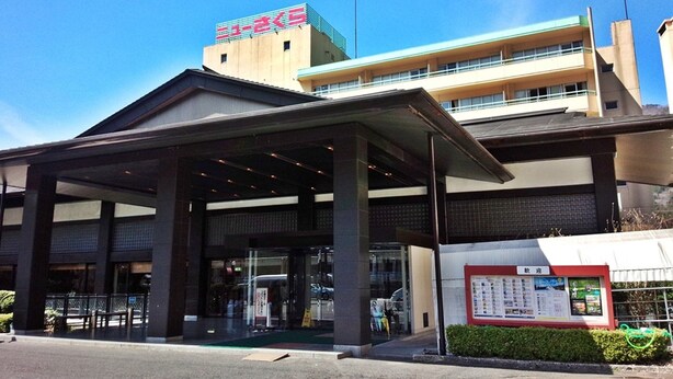 Entrada de hotel con un área de espera techada, mostrador de recepción a la vista y un cartel informativo.