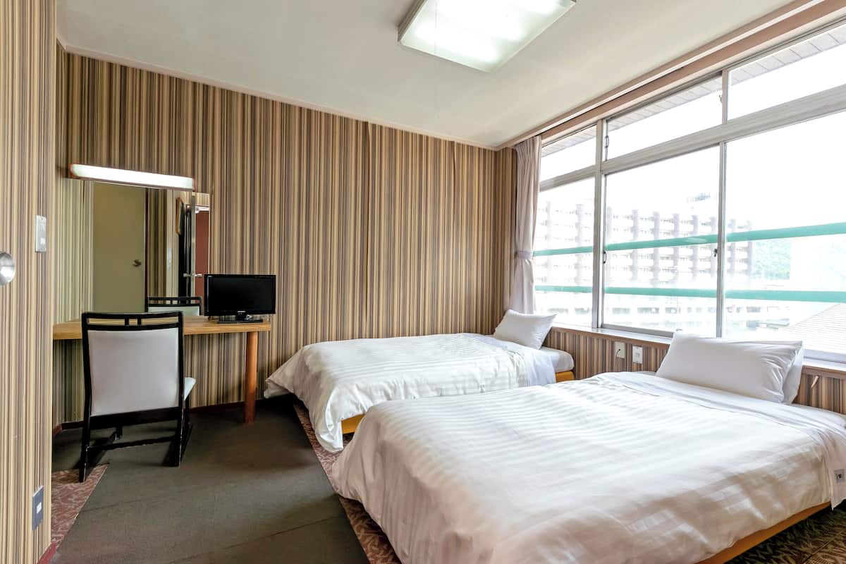 Ett hotellrum med två sängar, ett skrivbord med en tv, en stol och ett stort fönster.