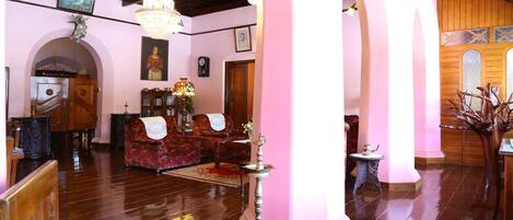 A spacious living room with a wooden floor, a red sofa, a chandelier, and a decorative tree.